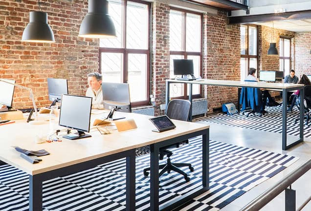 Kantoorwerkplek in creatieve en inspirerende flexwerken omgeving met grote ramen en industriële details.